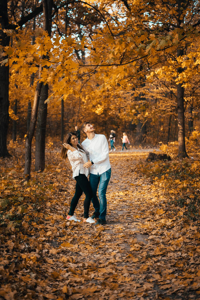 vrolijk jong koppel staan en knuffelen in de herfst bos - Foto, afbeelding