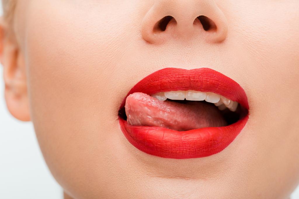 обрізаний вид жінки з червоною помадою облизуючи губи ізольовані на білому
  - Фото, зображення