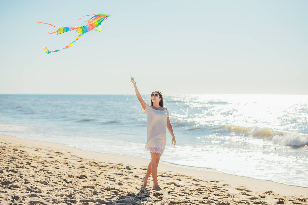 atraktivní veselá mladá žena drží barevné draka a chůzi na písečné pláži - Fotografie, Obrázek