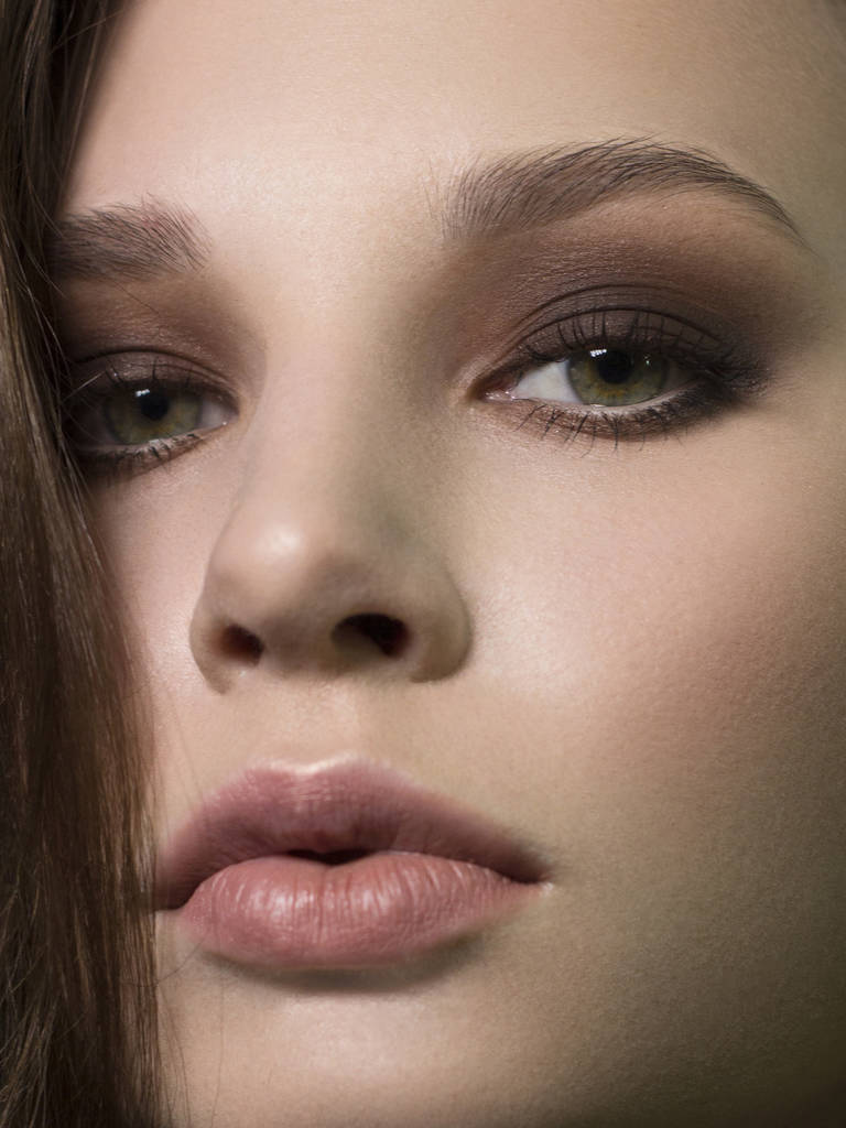 Κοντινό πορτρέτο του προσώπου αγνότητας της όμορφης γυναίκας με σκούρο μαύρο smoky-eyes make-up, γυμνά γεμάτα χείλη. Σέξι μοντέλο με καθαρό λαμπερό δέρμα, καθαρή επιδερμίδα - Φωτογραφία, εικόνα