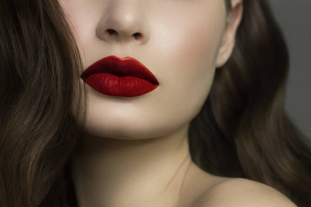 Close-up van de lippen van de vrouw met mode natuurlijke rode lippenstift make-up. Macro sexy bleke lipgloss make-up. Zachte zuivere huid en golvend brunet haar. Cosmetologie, Spa, toename van de lippen - Foto, afbeelding