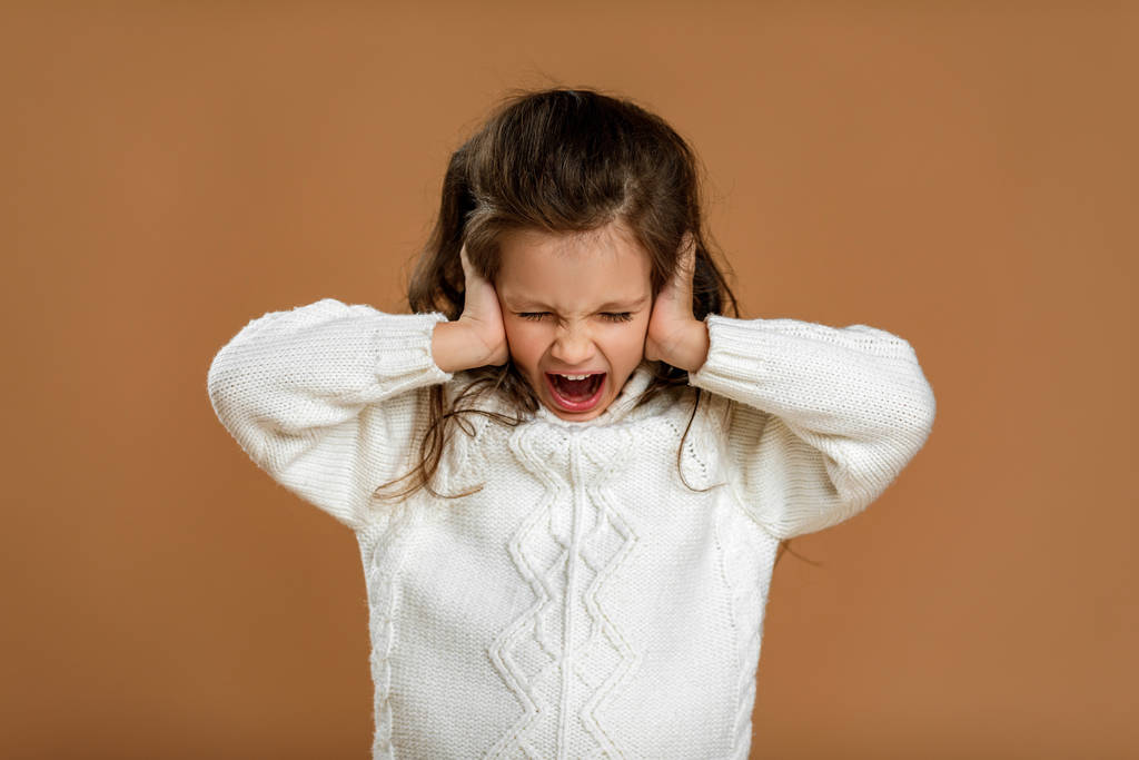 schattig krullend klein meisje in wit trui is sluiten haar oren - Foto, afbeelding