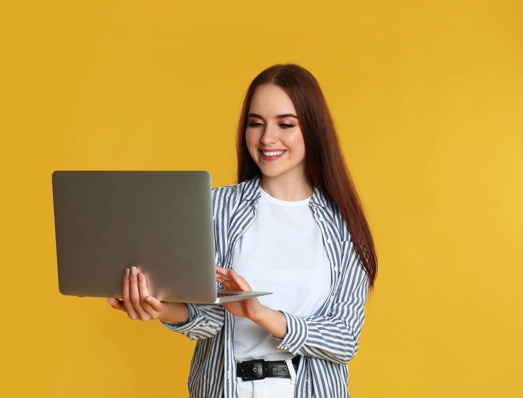 Šťastná žena s moderním notebookem na žlutém pozadí - Fotografie, Obrázek