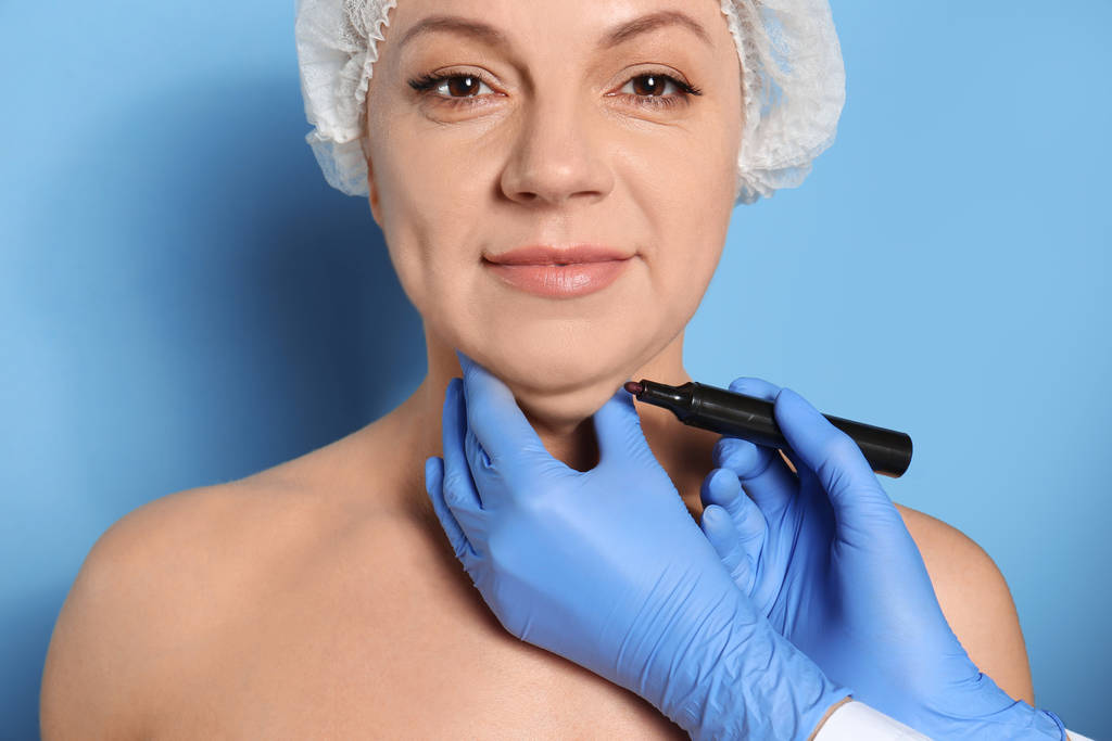 Хирург с маркером готовит женщину к операции против голубого цвета b
 - Фото, изображение