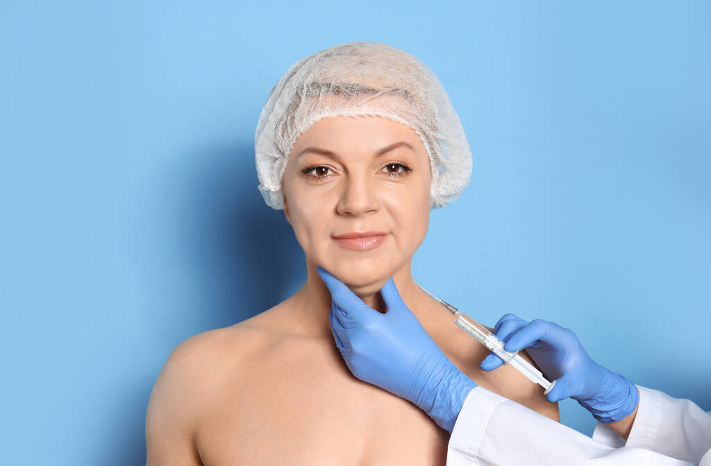 Starší žena s dvojitou bradou dostává injekci na modrý backgr - Fotografie, Obrázek