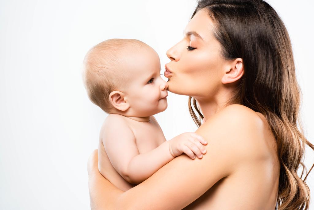 portrait of attractive naked mother hugging and kissing baby boy, isolated on white - Photo, Image