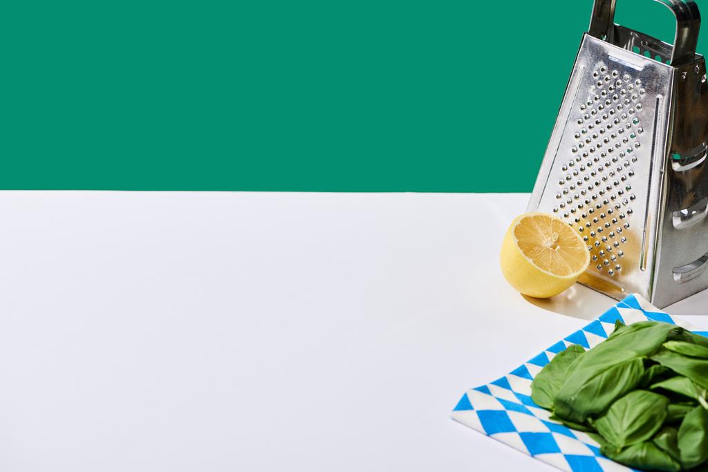 citron, listy bazalky a struhadlo na bílém stole izolované na zeleni - Fotografie, Obrázek