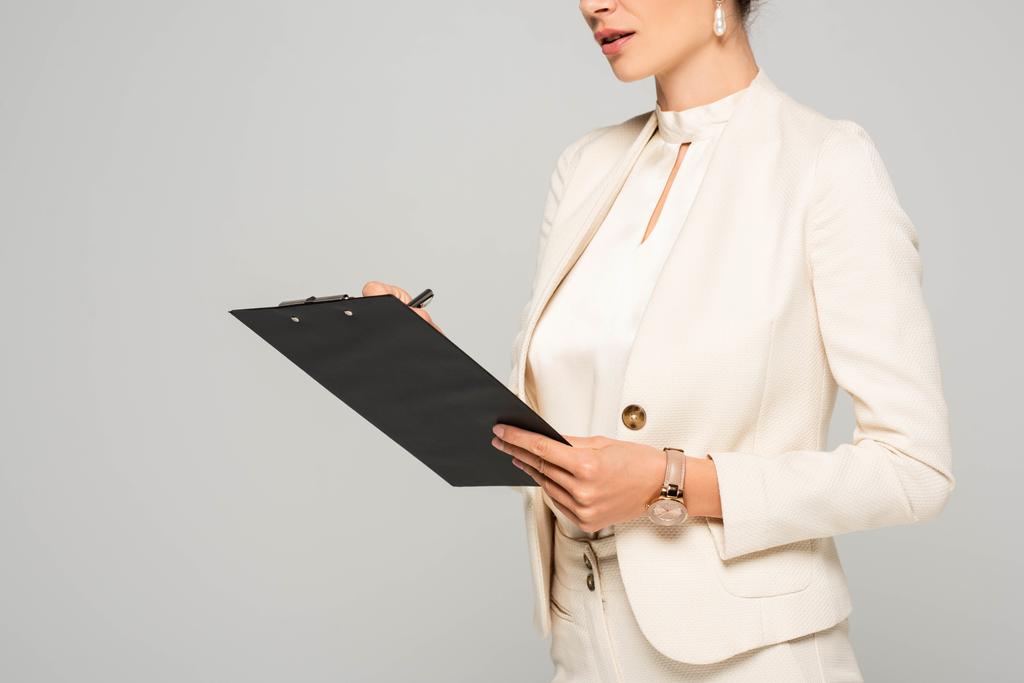 cropped view of businesswoman in white suit writing in clipboard, isolated on grey - Photo, Image