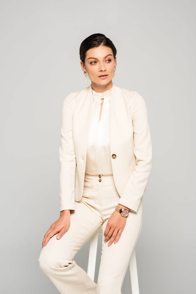 елегантна бізнес-леді в білому костюмі, сидить на табуреті, ізольована на сірому
 - Фото, зображення