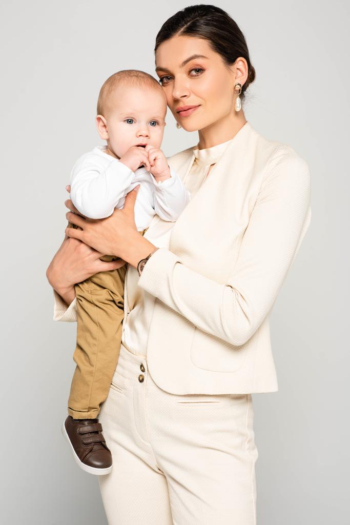 zakenvrouw houden schattig baby jongen op handen, geïsoleerd op grijs - Foto, afbeelding