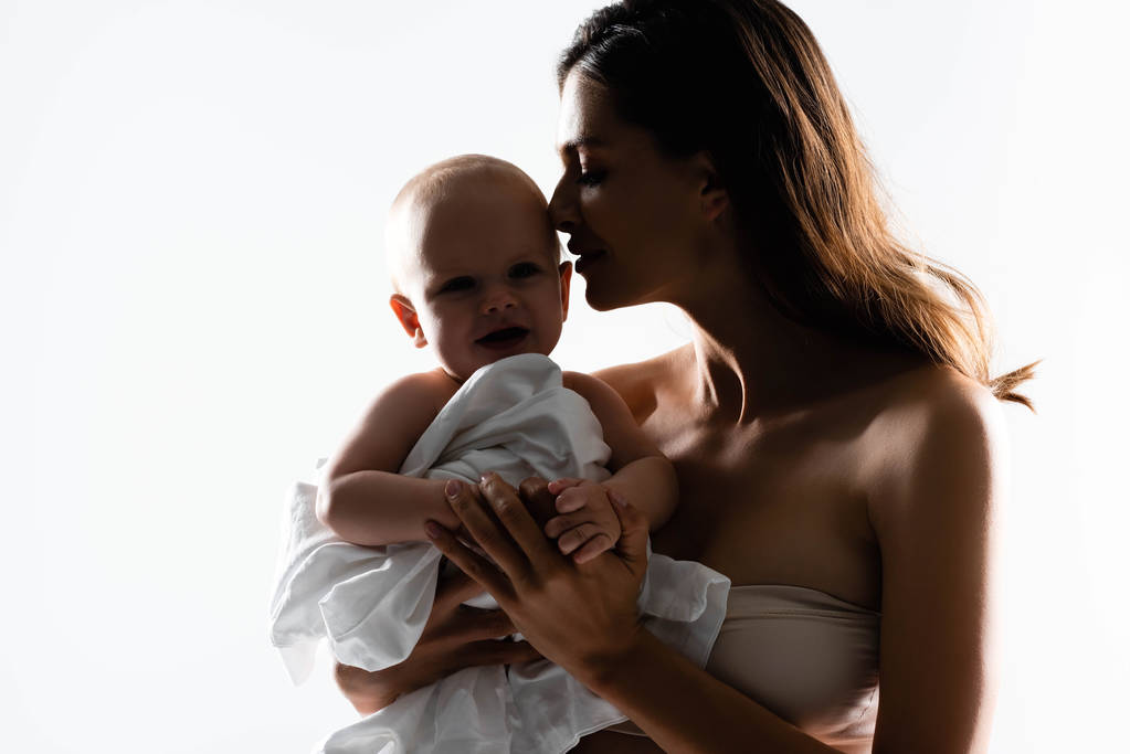 Silhouette einer zarten Mutter, die einen kleinen Jungen auf Händen hält, isoliert auf weiß - Foto, Bild