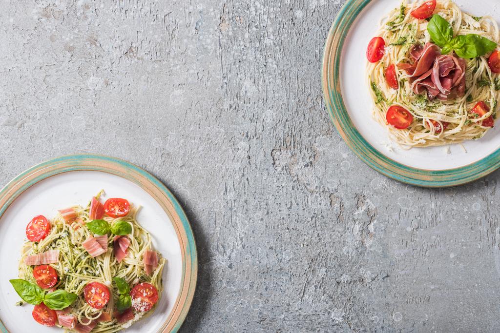 ylhäältä näkymä Pappardelle tomaatit, basilika ja prosciutto lautasilla harmaalla pinnalla
 - Valokuva, kuva