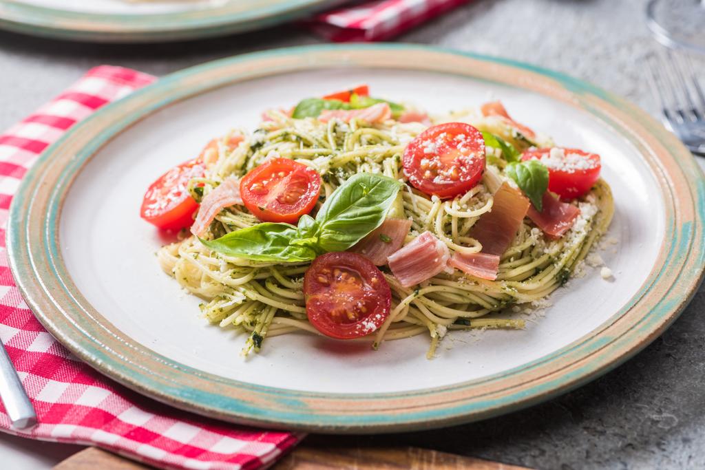 Pappardelle tomaattien, basilikan ja prosciutton kanssa harmaalla pinnalla ruudullisella lautasliinalla
 - Valokuva, kuva