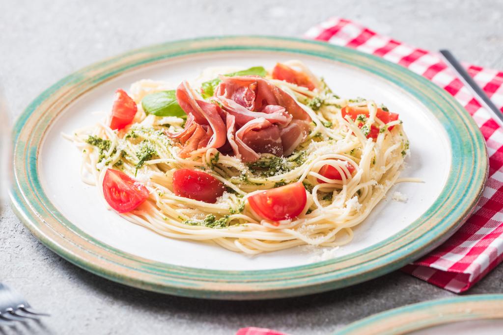Pappardelle con tomates, albahaca y jamón sobre superficie gris con servilleta a cuadros
 - Foto, Imagen