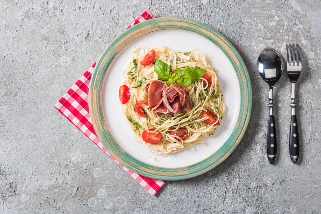 Pappardelle 'e servis edilen domatesli, fesleğenli ve prosciutto ekose peçeteli gri yüzey çatal bıçaklı. - Fotoğraf, Görsel