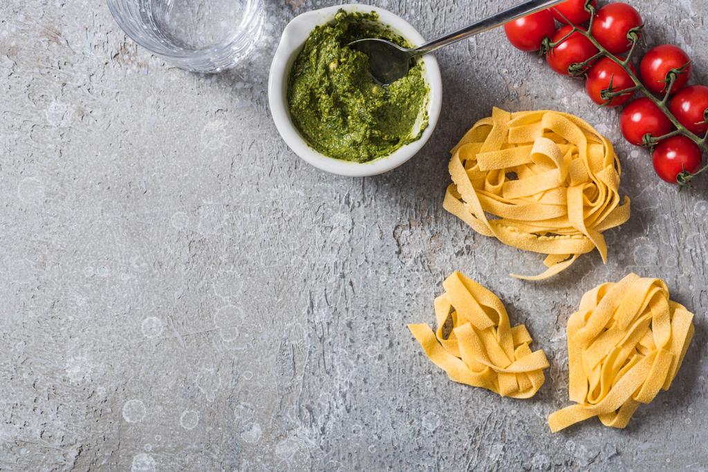 top view of raw Pappardelle near tomatoes, water and pesto sauce on grey surface - Photo, Image