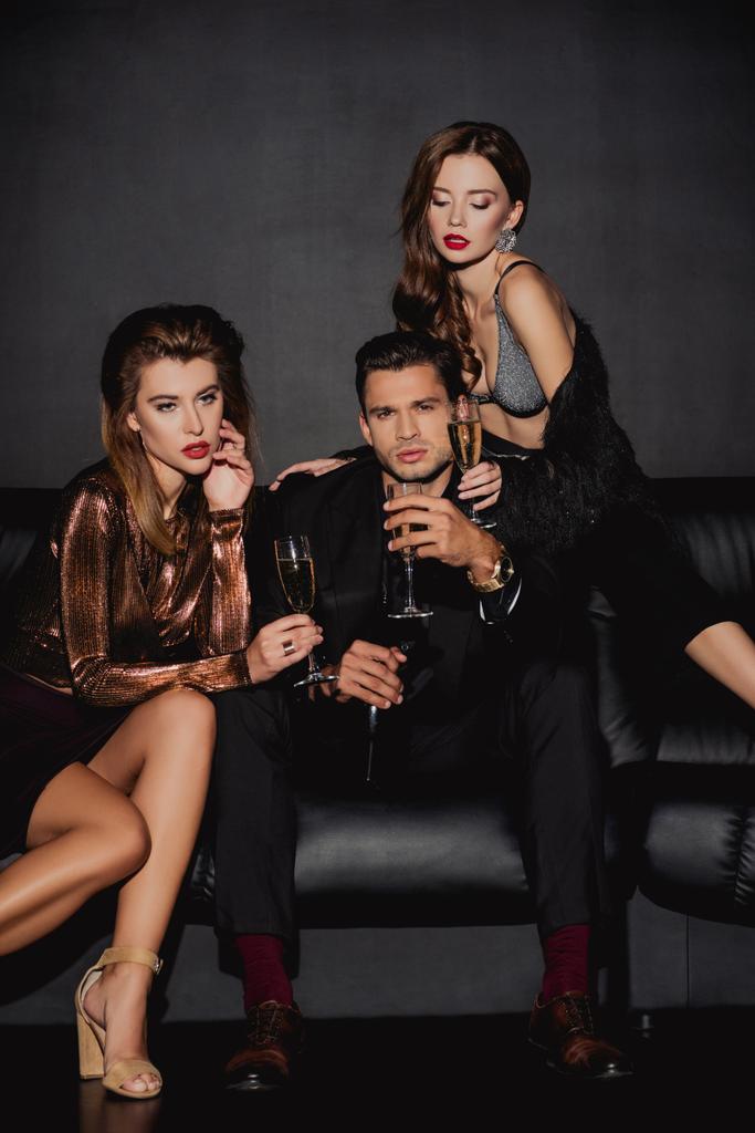 aantrekkelijke vrouwen en knappe man met champagne glazen geïsoleerd op zwart - Foto, afbeelding