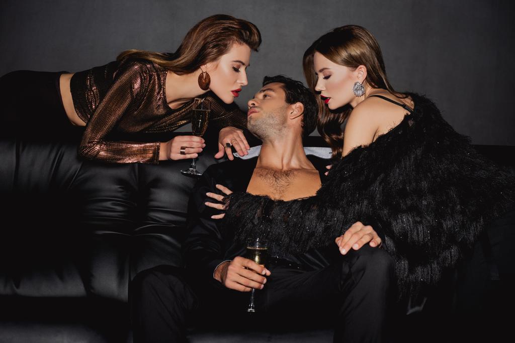 attraktive Frauen küssen schönen Mann mit Champagnerglas isoliert auf schwarz - Foto, Bild