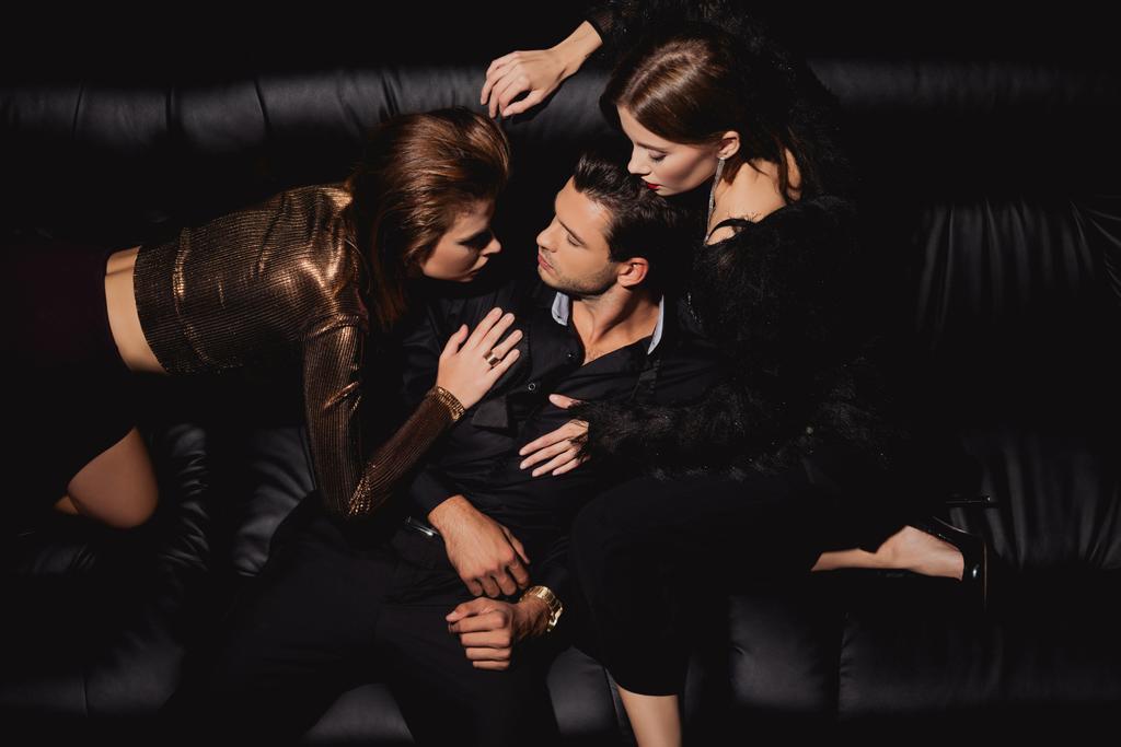 top view of attractive women kissing and hugging handsome man on black background  - Photo, Image