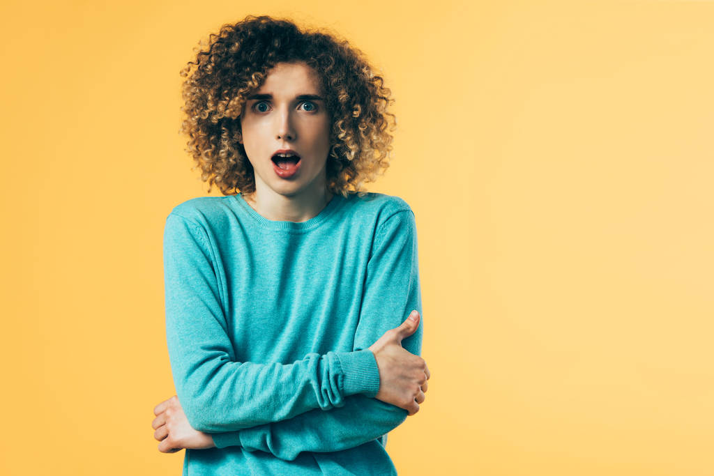 shocked curly teenager with open mouth and crossed arms isolated on yellow - Photo, Image
