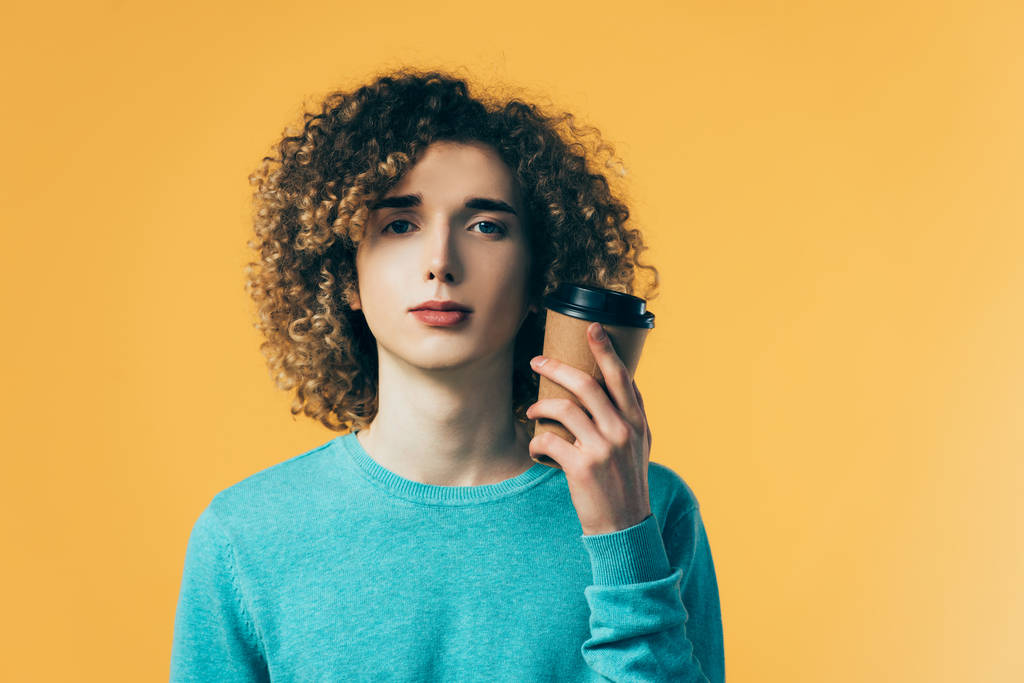 kudrnatý teenager drží kávu v papírovém šálku izolované na žluté - Fotografie, Obrázek
