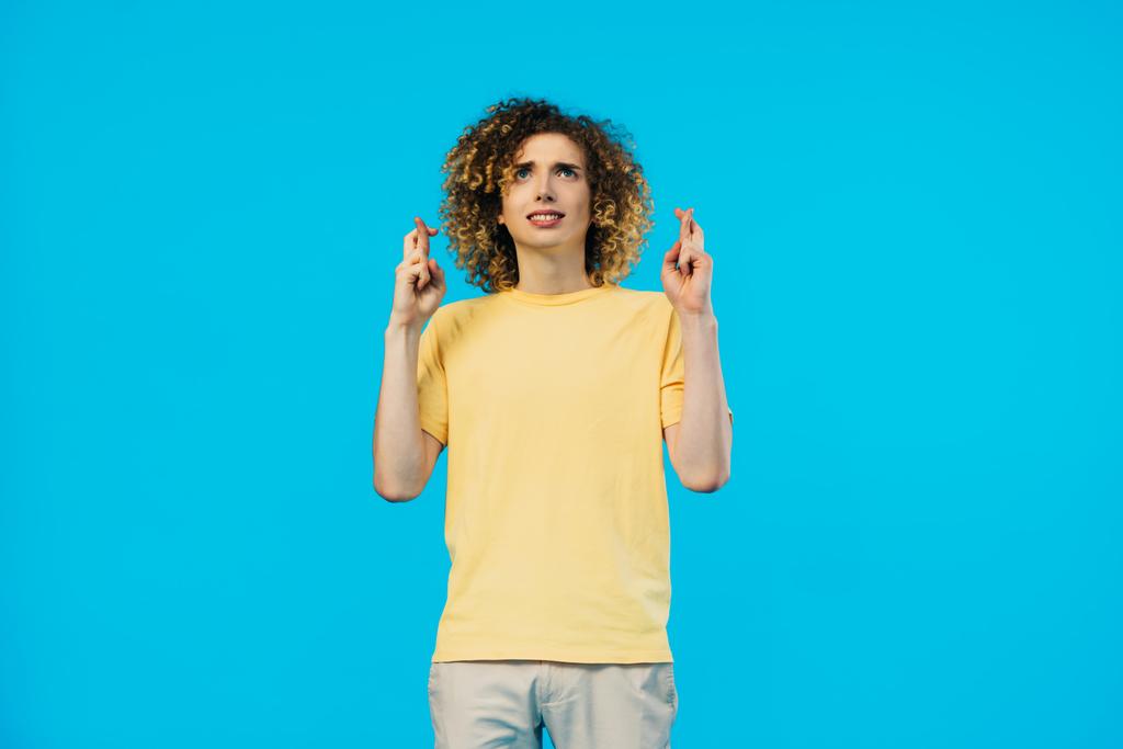bezorgde krullende tiener met gekruiste vingers geïsoleerd op blauw - Foto, afbeelding