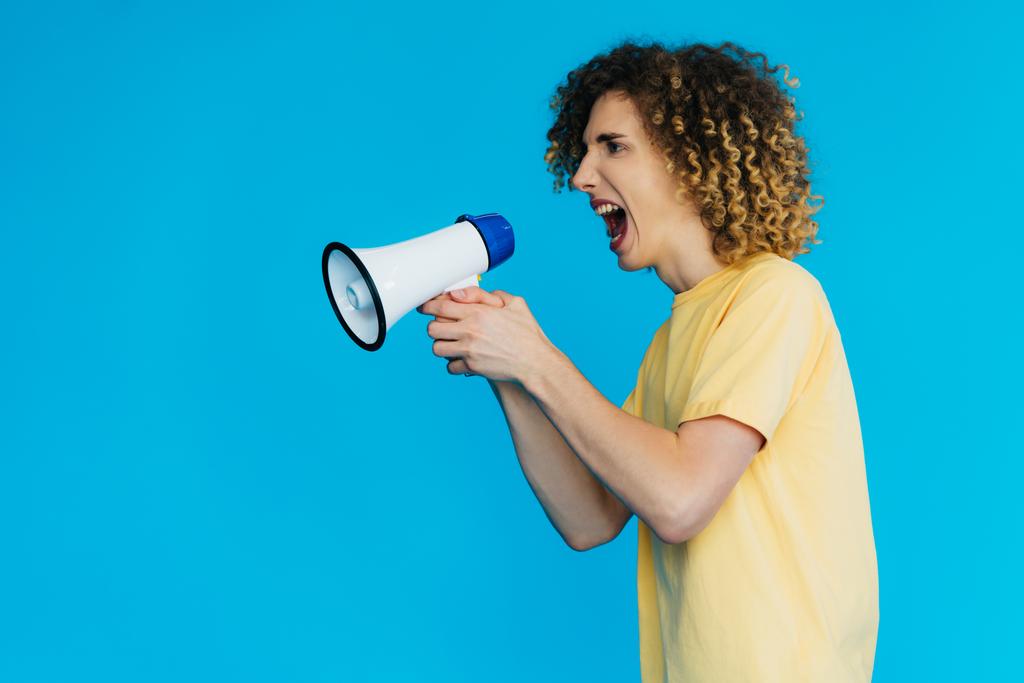 side view of angry curly teenager screaming in loudspeaker isolated on blue - Photo, Image