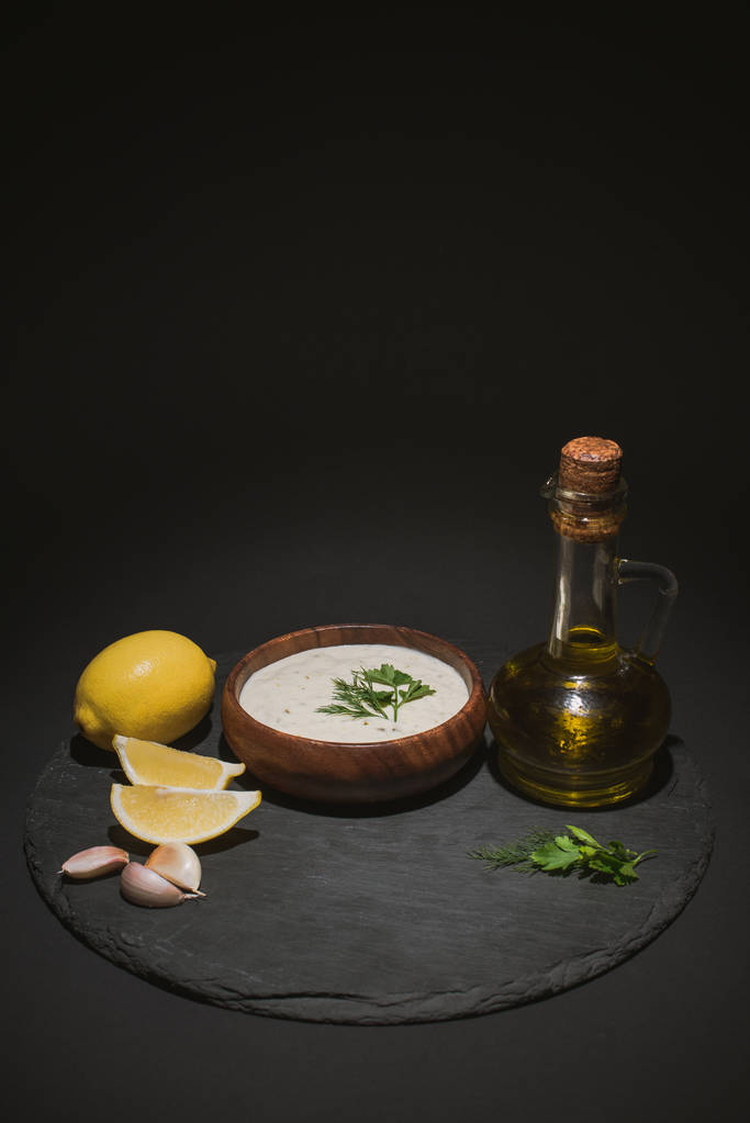 Molho tzatziki grego tradicional com azeite e ingredientes sobre placa escura sobre fundo preto
 - Foto, Imagem