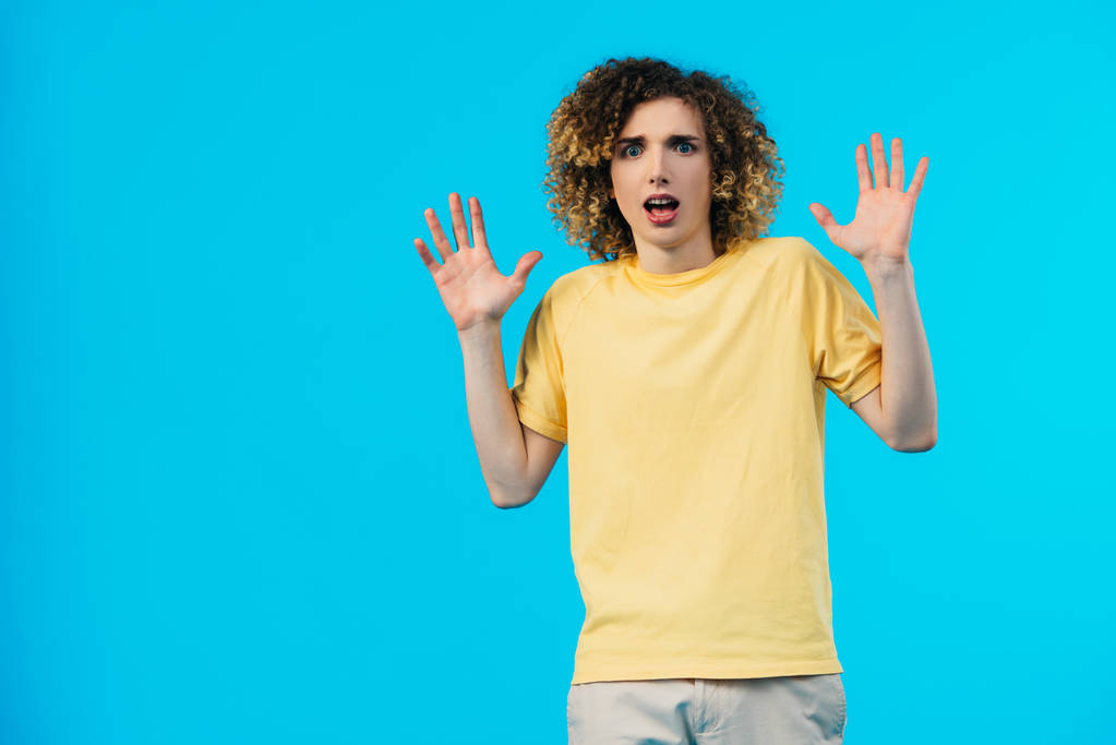asustado rizado adolescente mostrando manos aisladas en azul
 - Foto, Imagen