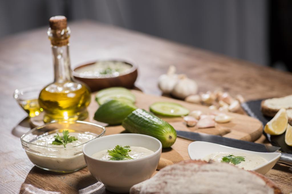 Heerlijke tzatziki saus met ingrediënten en olijfolie op houten keukentafel  - Foto, afbeelding
