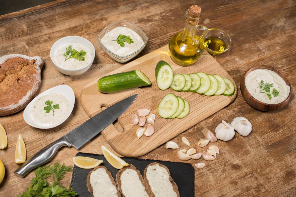 Čerstvé ingredience s olivovým olejem a tzatziki omáčkou v miskách na dřevěném stole  - Fotografie, Obrázek