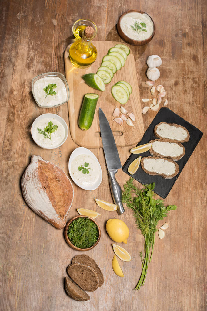 Κάτοψη της σάλτσας τζατζίκι με υλικά και ψωμί σε ξύλινο τραπέζι - Φωτογραφία, εικόνα