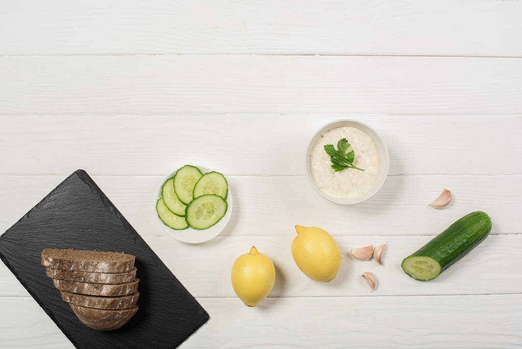 Top view of tzatziki sauce with bread on black board on white wooden background - Photo, Image