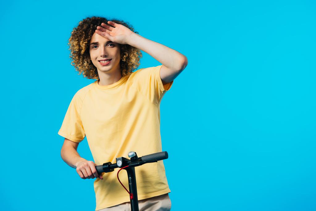 heureux adolescent bouclé équitation scooter électrique isolé sur bleu
 - Photo, image