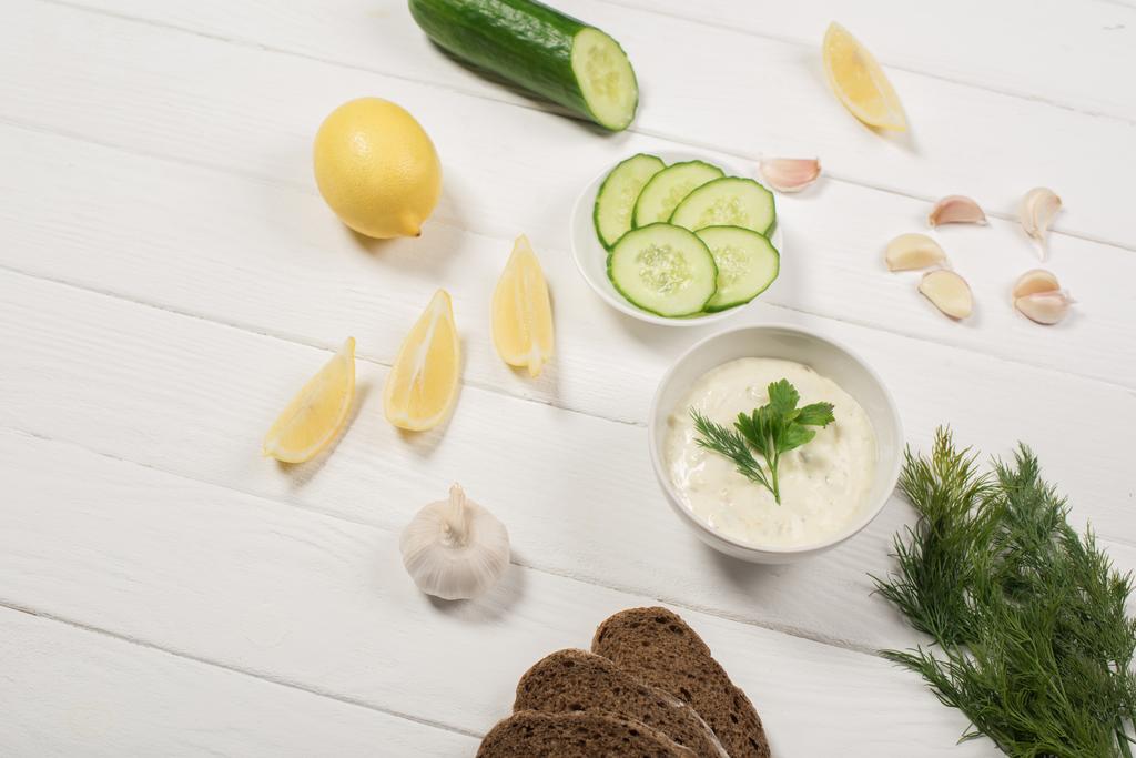 Tzatziki sauce in bowl with fresh ingredients and bread on white wooden background - Photo, Image