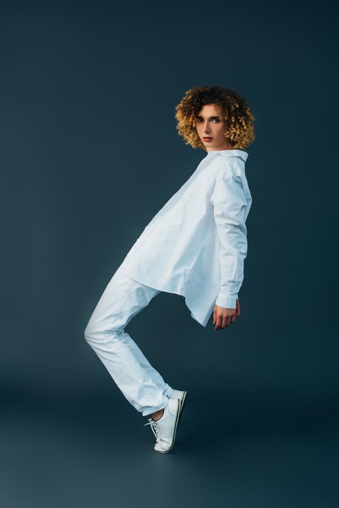 side view of curly teenager in total white outfit posing on tiptoe isolated on green - Photo, Image