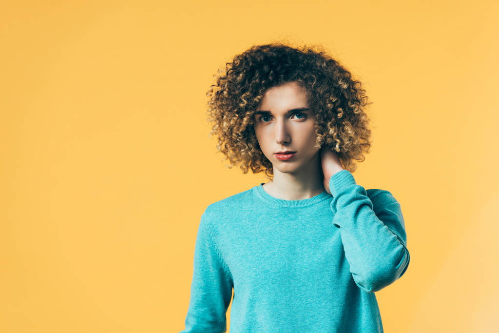 curly teenager touching neck isolated on yellow - Photo, Image