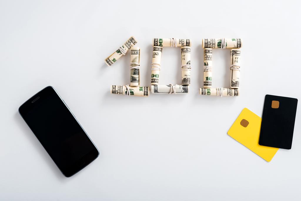 κορυφαία άποψη του smartphone με κενή οθόνη κοντά σε ρολά μετρητών και πρότυπα πιστωτικών καρτών σε λευκό  - Φωτογραφία, εικόνα