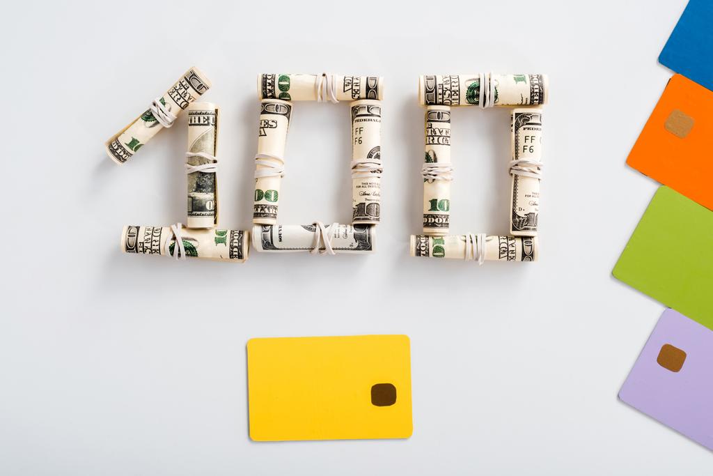 κορυφαία άποψη των τραπεζογραμματίων εκατό δολαρίων σε ρολά μετρητών κοντά πολύχρωμα πρότυπα πιστωτικών καρτών σε λευκό  - Φωτογραφία, εικόνα