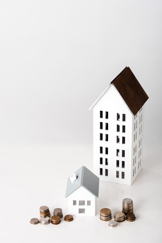 χάρτινα σπίτια κοντά σε στοίβες με κέρματα σε λευκό  - Φωτογραφία, εικόνα