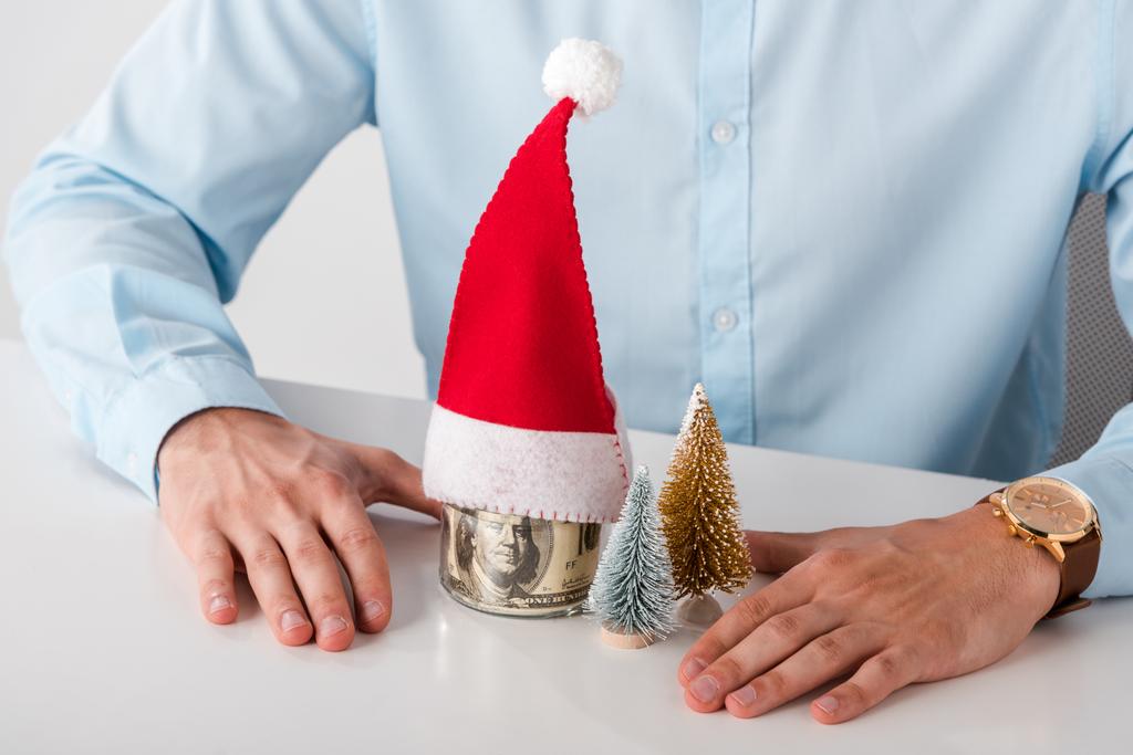 cropped view of man near glass jar with money and santa hat isolated on white  - Photo, Image
