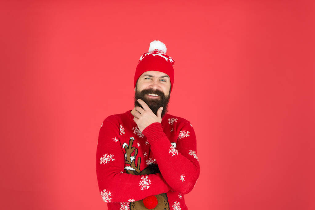 Bearded face close up red background. Cold days. Winter holidays. Man bearded hipster wear winter knitted hat. Barbershop and facial hair. Winter skin care. Guy wearing winter clothes and accessory - Photo, Image