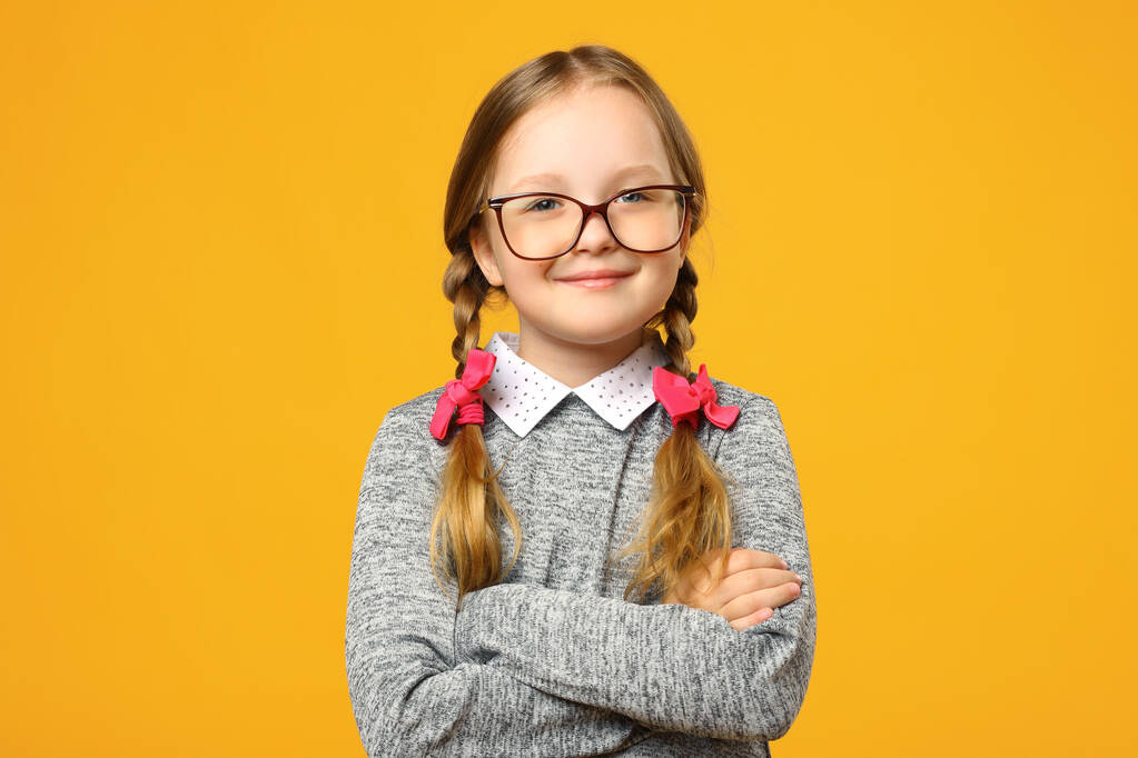 Portrait rapproché d'une drôle de petite fille en lunettes sur fond jaune. Enfant écolière plié les bras et regarde dans la caméra
 - Photo, image