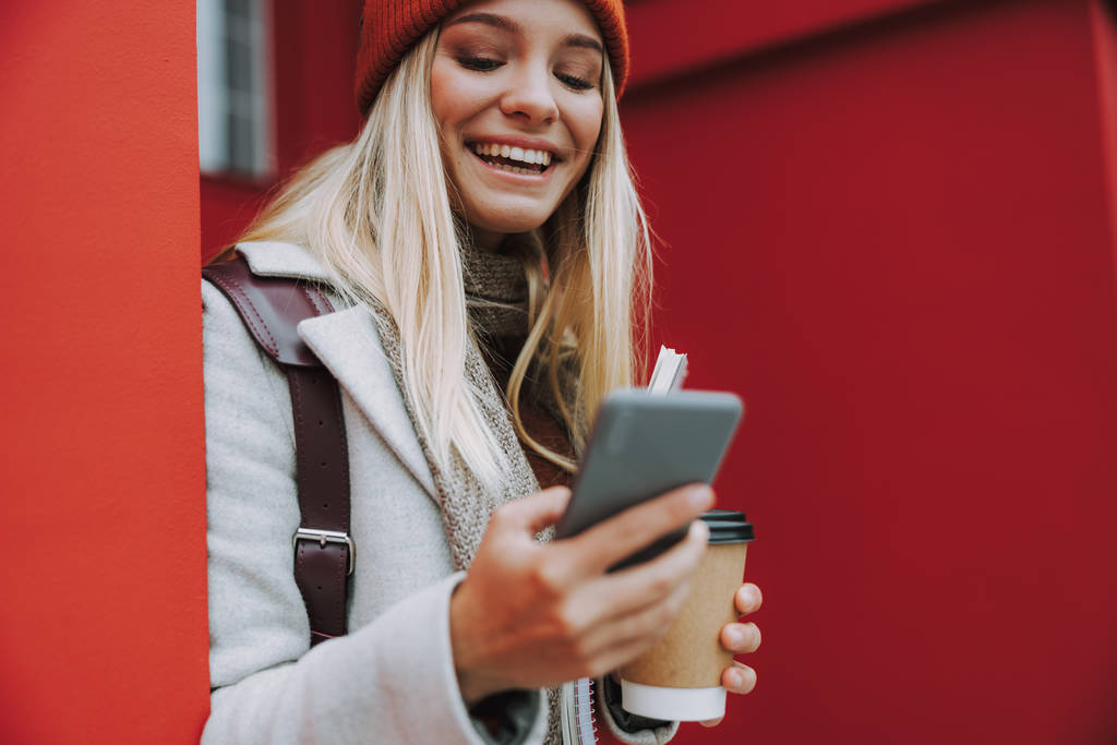Молодая женщина с кофе с помощью смартфона и широко улыбаясь
 - Фото, изображение