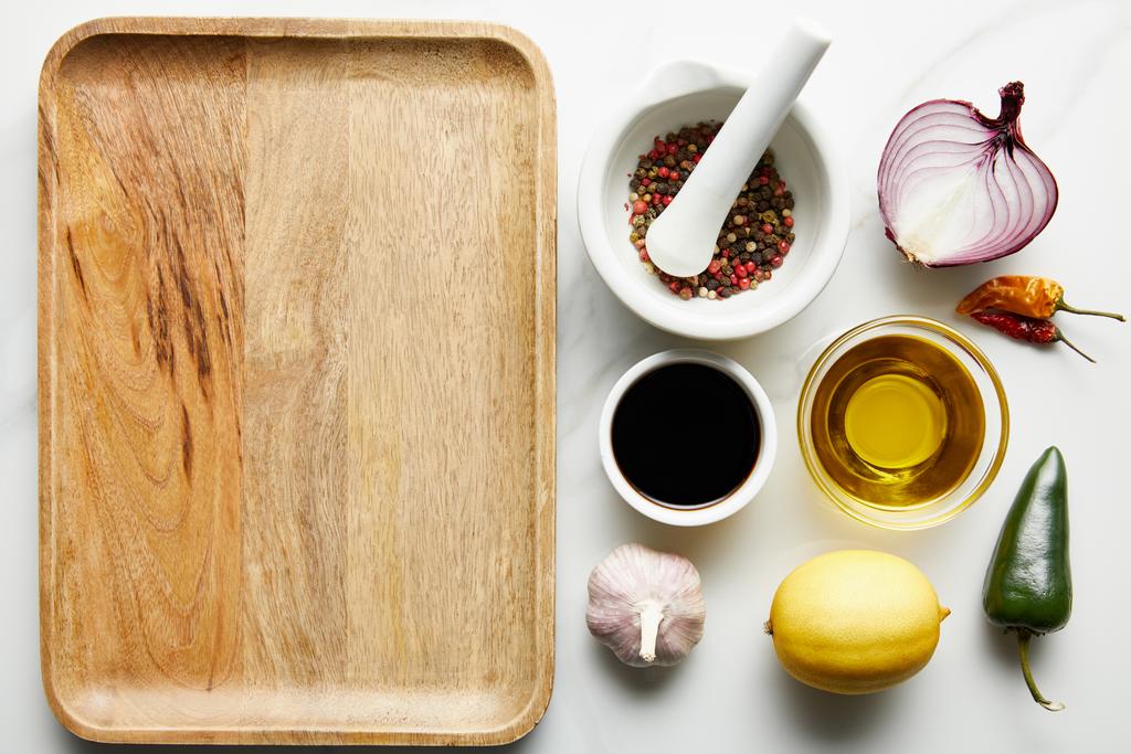 Horní pohled na sójovou omáčku, olivový olej s kořením a citrón vedle dřevěného talíře na mramorovém pozadí - Fotografie, Obrázek