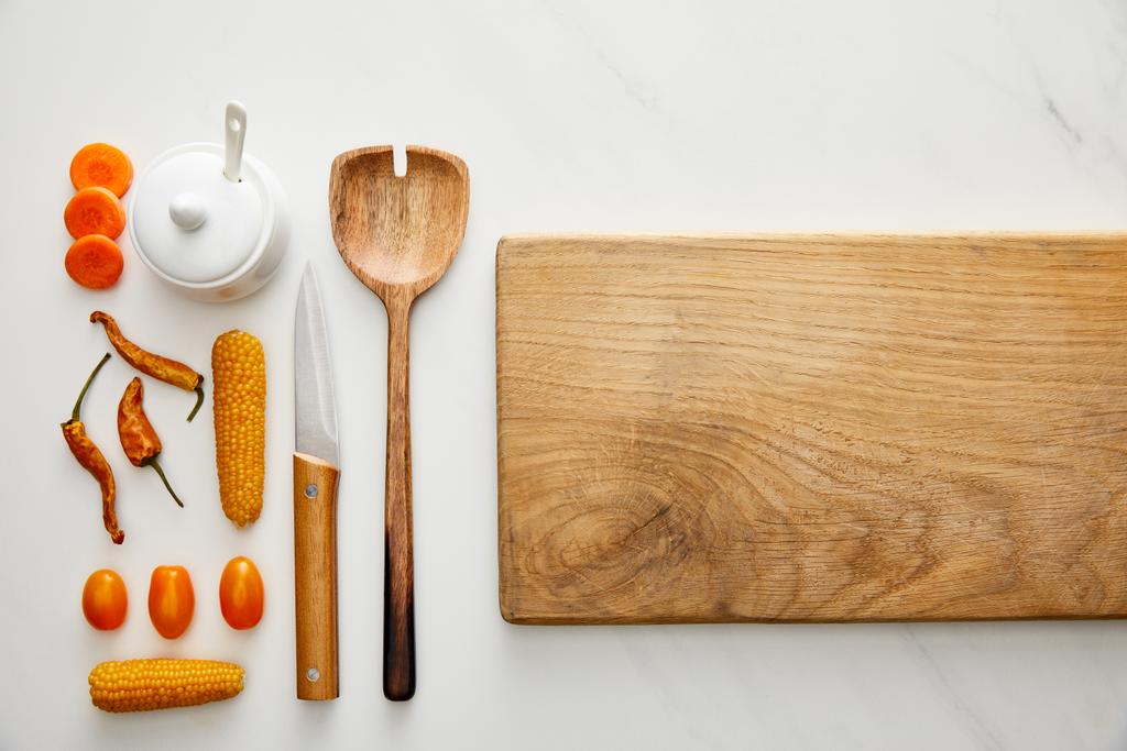 Vista superior de la tabla de cortar con utensilios de cocina y verduras sobre fondo de mármol
 - Foto, Imagen