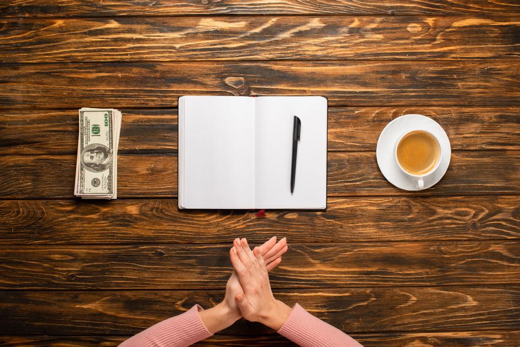 vue recadrée de femme d'affaires se frottant les mains tout en se préparant à écrire nouvelle résolution de l'année près de billets en dollars et tasse à café sur un bureau en bois
 - Photo, image