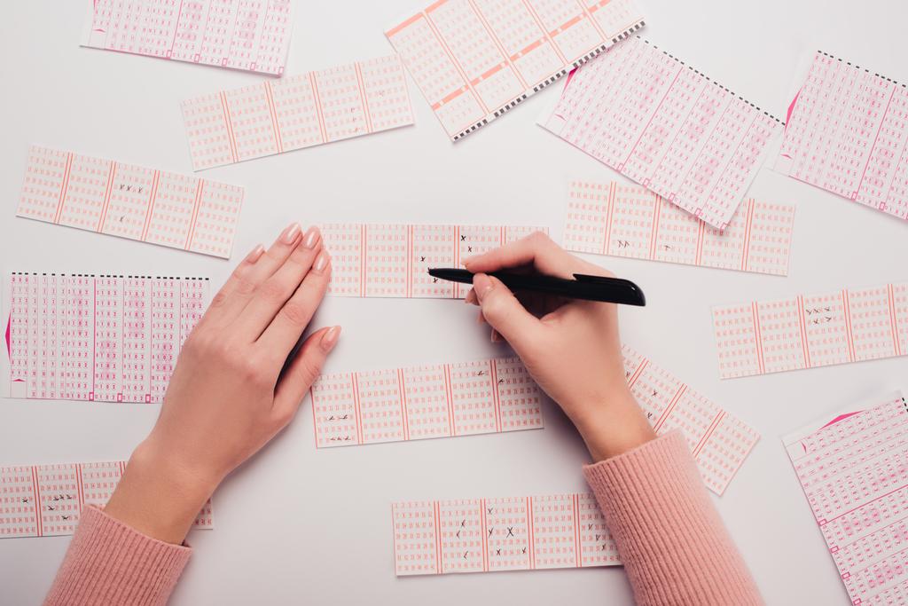 частичный вид женщины, маркирующей номера на лотерейных билетах на белом столе
 - Фото, изображение