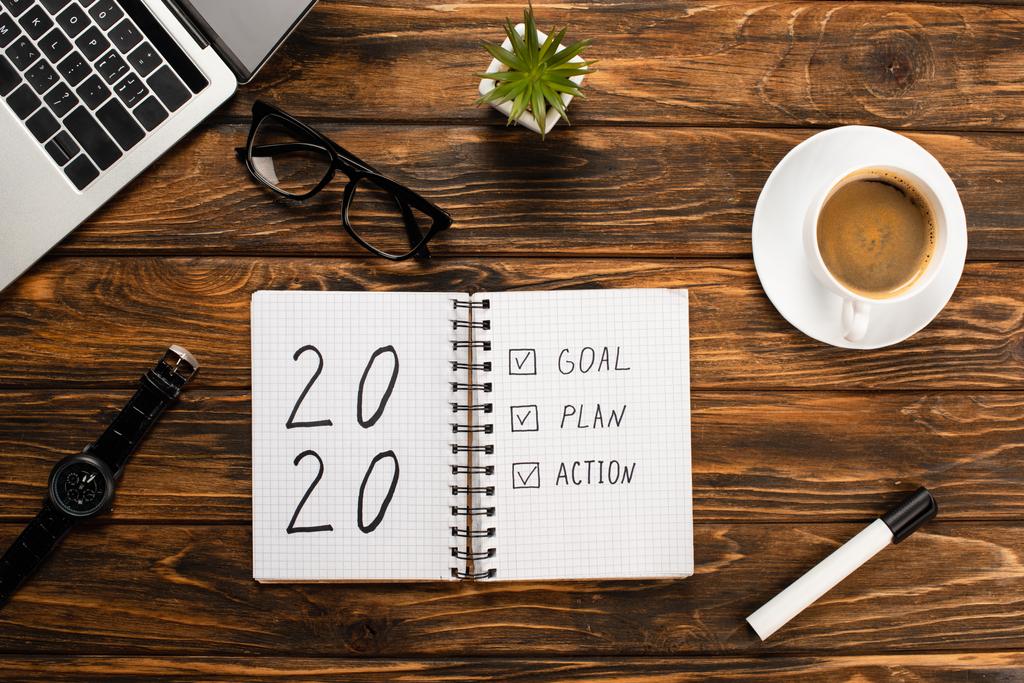 notebook s 2020, cíl, plán, akční písmo, notebook, šálek kávy, plstěné pero, brýle, náramkové hodinky a rostliny na dřevěném stole - Fotografie, Obrázek