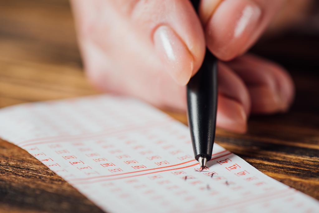 крупним планом рука гравця, що маркує номери в лотерейному квитку з ручкою на дерев'яному столі
 - Фото, зображення